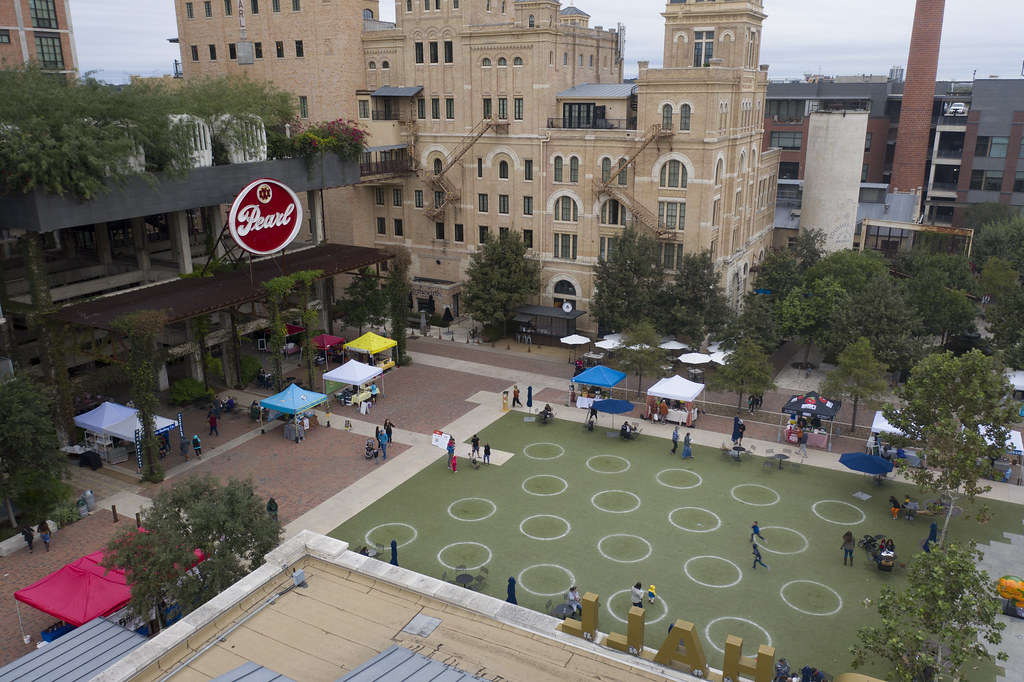 Aerial view of a public space with people gathered around tents and a historic building in the background.